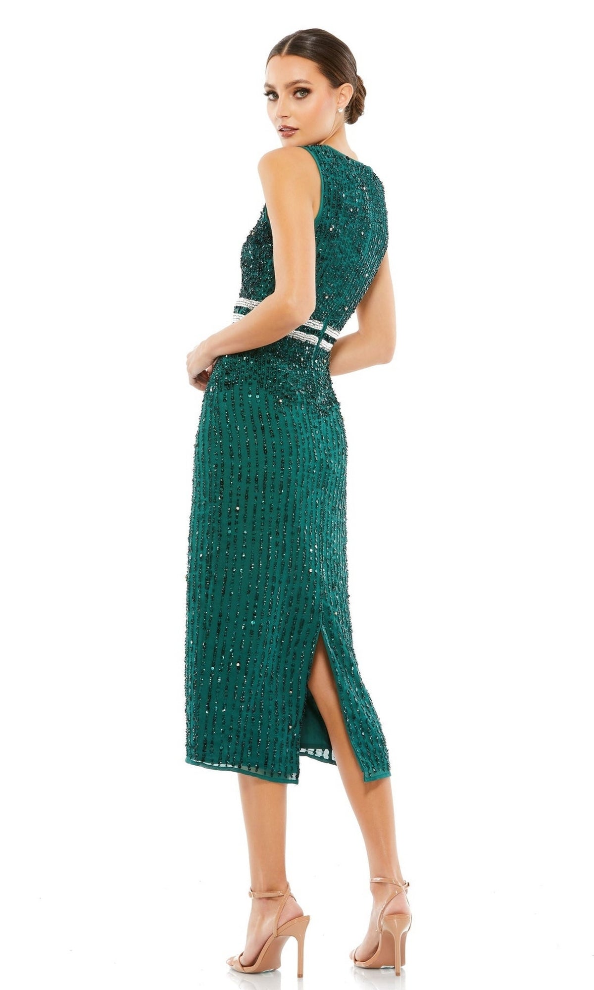 A woman in the Mac Duggal 10509 Short Sequin Wedding Guest Dress, featuring a sleeveless green design with a knee-length hem and back slit, stands in nude high-heeled sandals looking over her shoulder.